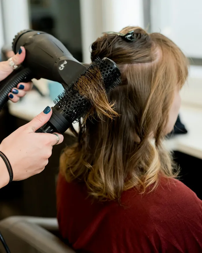 Shoulder-length brown hair being styled with a round brush and a hairdryer.