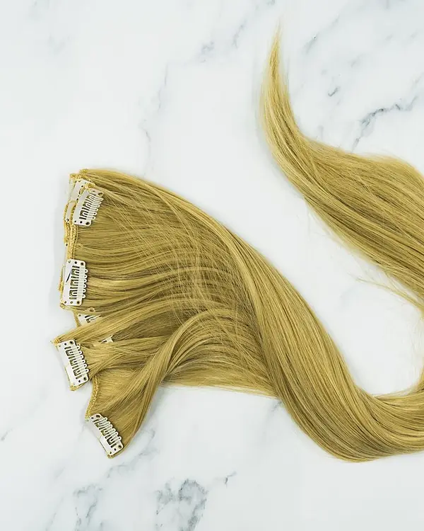 Blonde clip-in hair extensions laid out on marble.