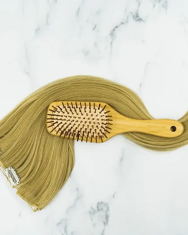 Clip-in extensions with a wooden paddle brush resting on top.