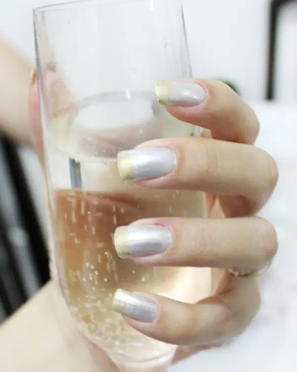 A neat manicure with silver tips, holding a glass of fizz.