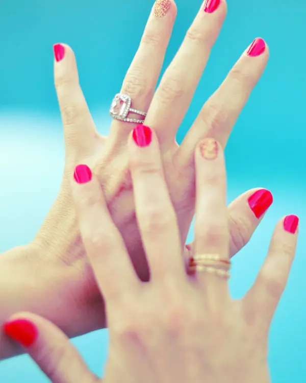Bright pink manicured nails with stacked rings.