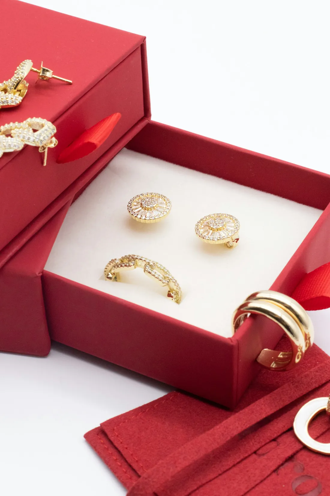 Gold studs and rings set out in an open red jewellery box.