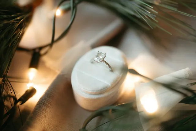 A diamond ring in a velvet box, with tree lights glowing behind it.