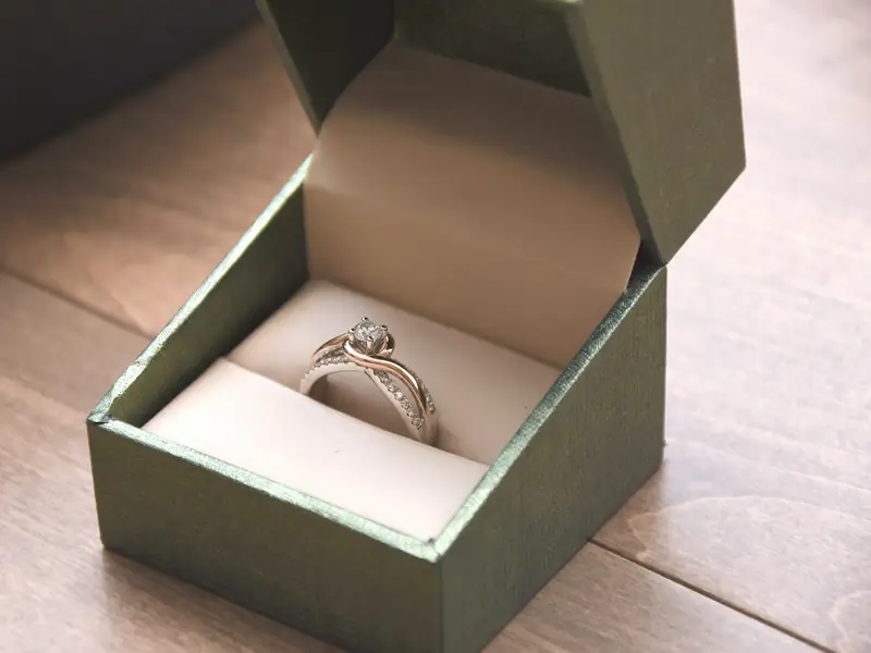 A diamond ring in an open green box on a wooden table.