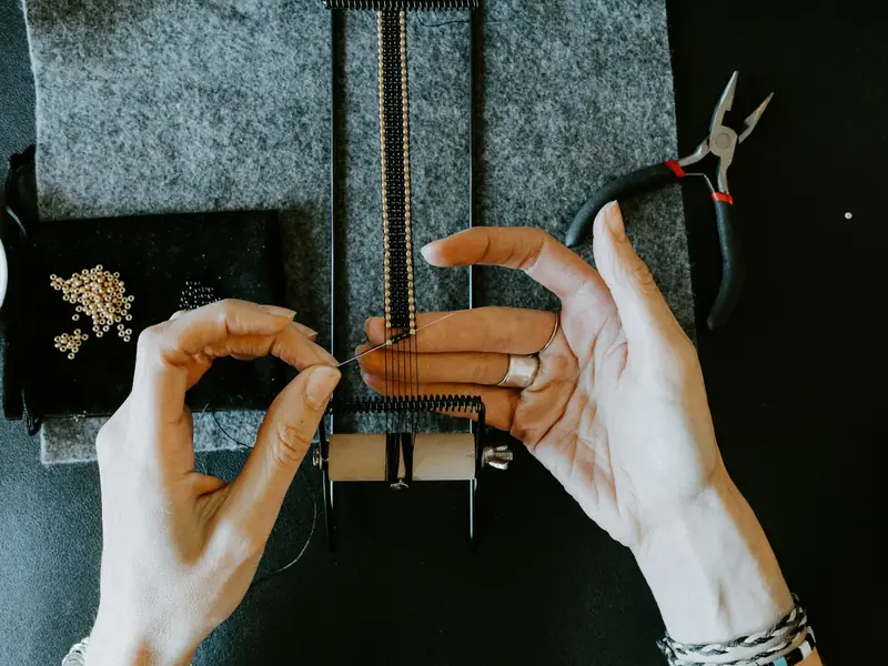 Hands threading beads at a workbench, with pliers close by.