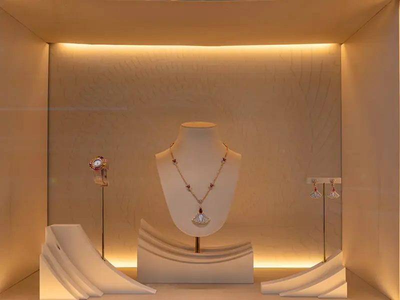 A necklace on a bust with earrings on either side, lit softly inside a showcase.