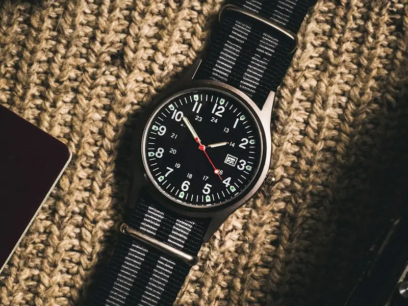 A black-dialled watch on a grey striped strap, resting on chunky knitwear.